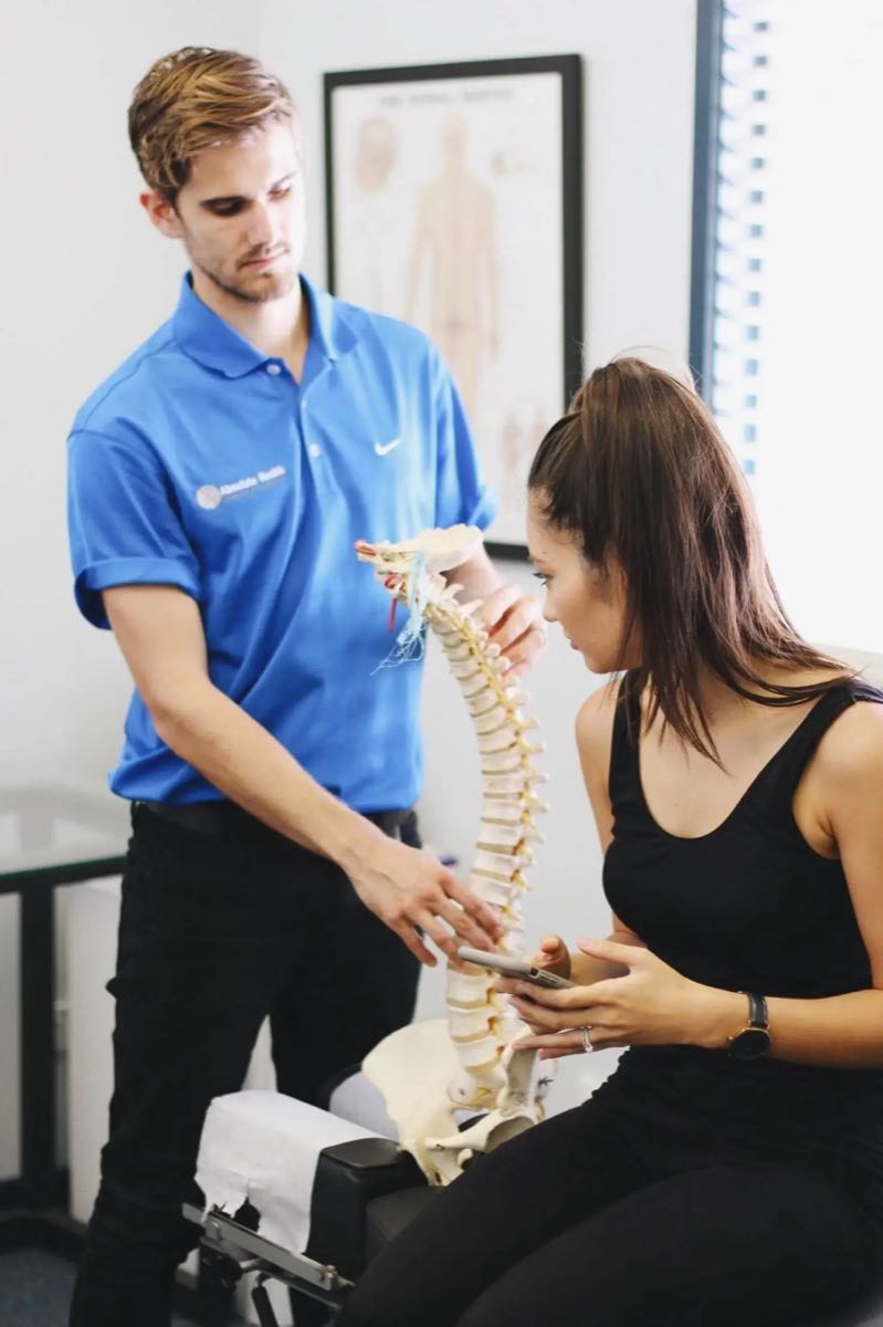 Chiropractor examining patient's spine with anatomical model, Absolute Health physiotherapy services.