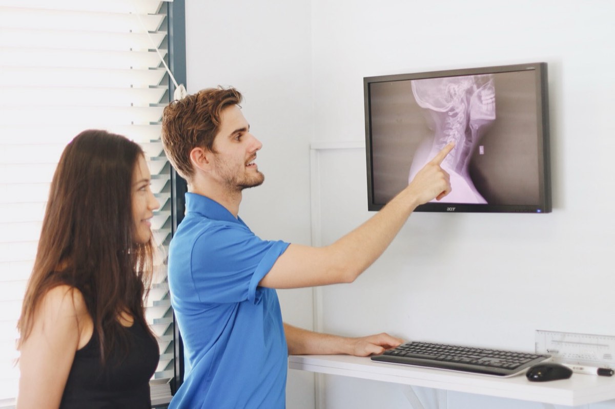 Absolute Health digital X-ray of neck displayed on screen, doctor pointing and discussing with patient.